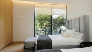 A modern bedroom with a large window, a bed, a bench, and a nightstand.