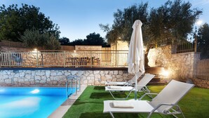 A swimming pool with artificial grass and lounge chairs, surrounded by stone walls and trees.