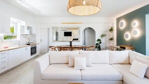 A modern kitchen with white cabinetry, a dining area with a wooden table and chairs, and a living room with a white sofa and a coffee table.
