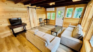 Un interior acogedor de cabaña con paredes de madera, un sofá, una mesa y un televisor.