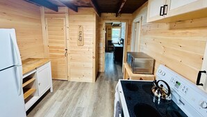 Una cocina compacta con paredes de madera, un refrigerador blanco, un microondas, una estufa y un hervidor.