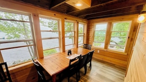 Una cabaña de madera con una mesa y sillas de comedor, amplias ventanas con vistas a un cuerpo de agua.