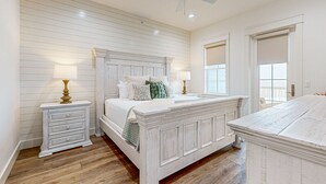 A bedroom with a large bed, two bedside tables, a ceiling fan, and a view of the outside. - Gorgeous family beach home with beach & gulf views, balconies,  pools, & golf (Port Aransas)