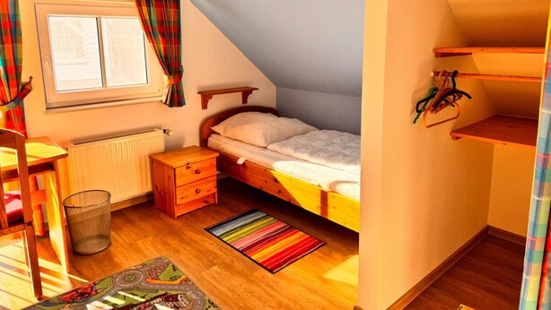 A cozy attic bedroom with a sloped ceiling, a wooden bed, a small desk, and a radiator. - Doppelhaushalfte in Burhave (Butjadingen)