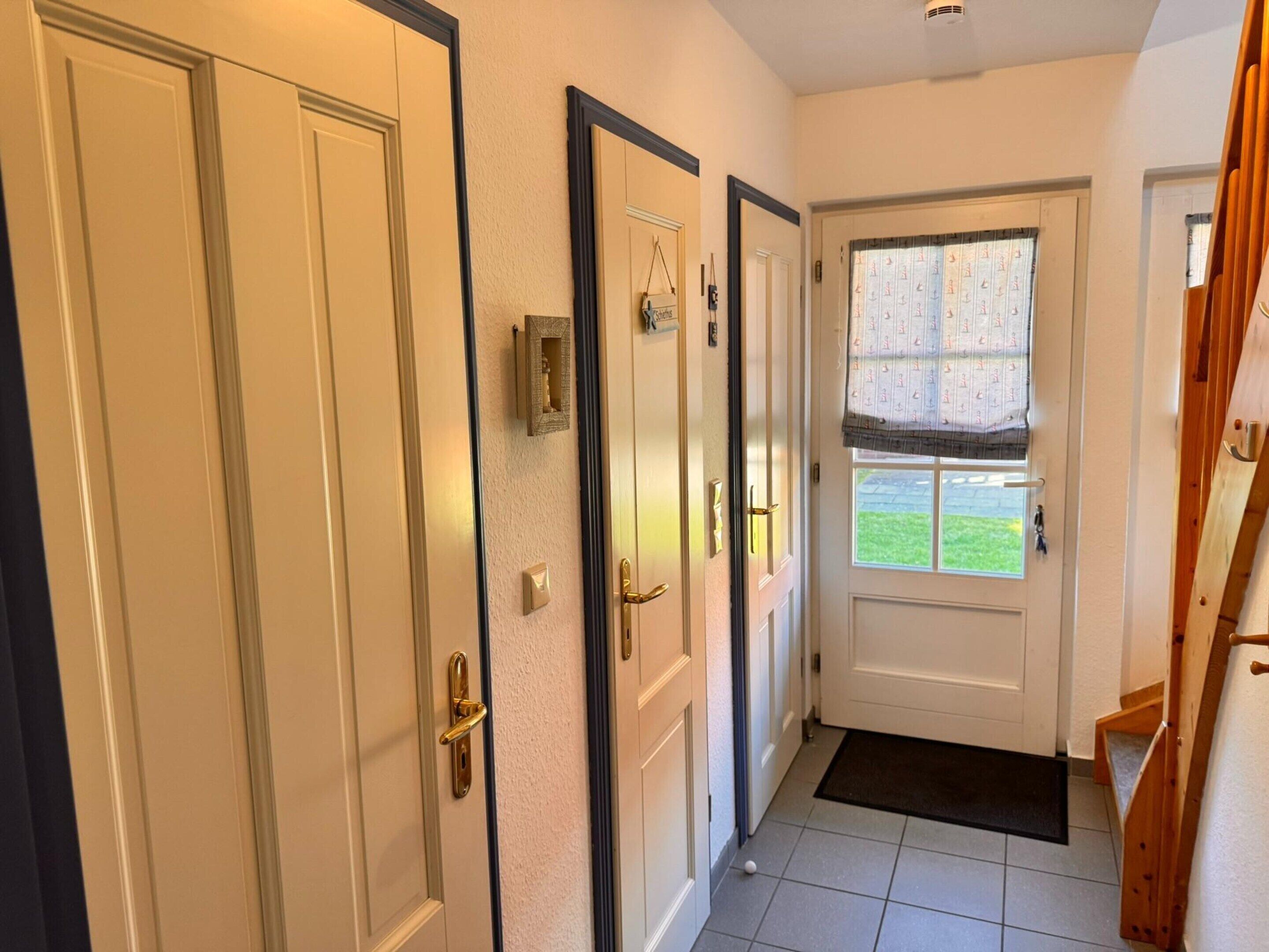 A hallway with three doors, a window with patterned curtains, and a wooden staircase.