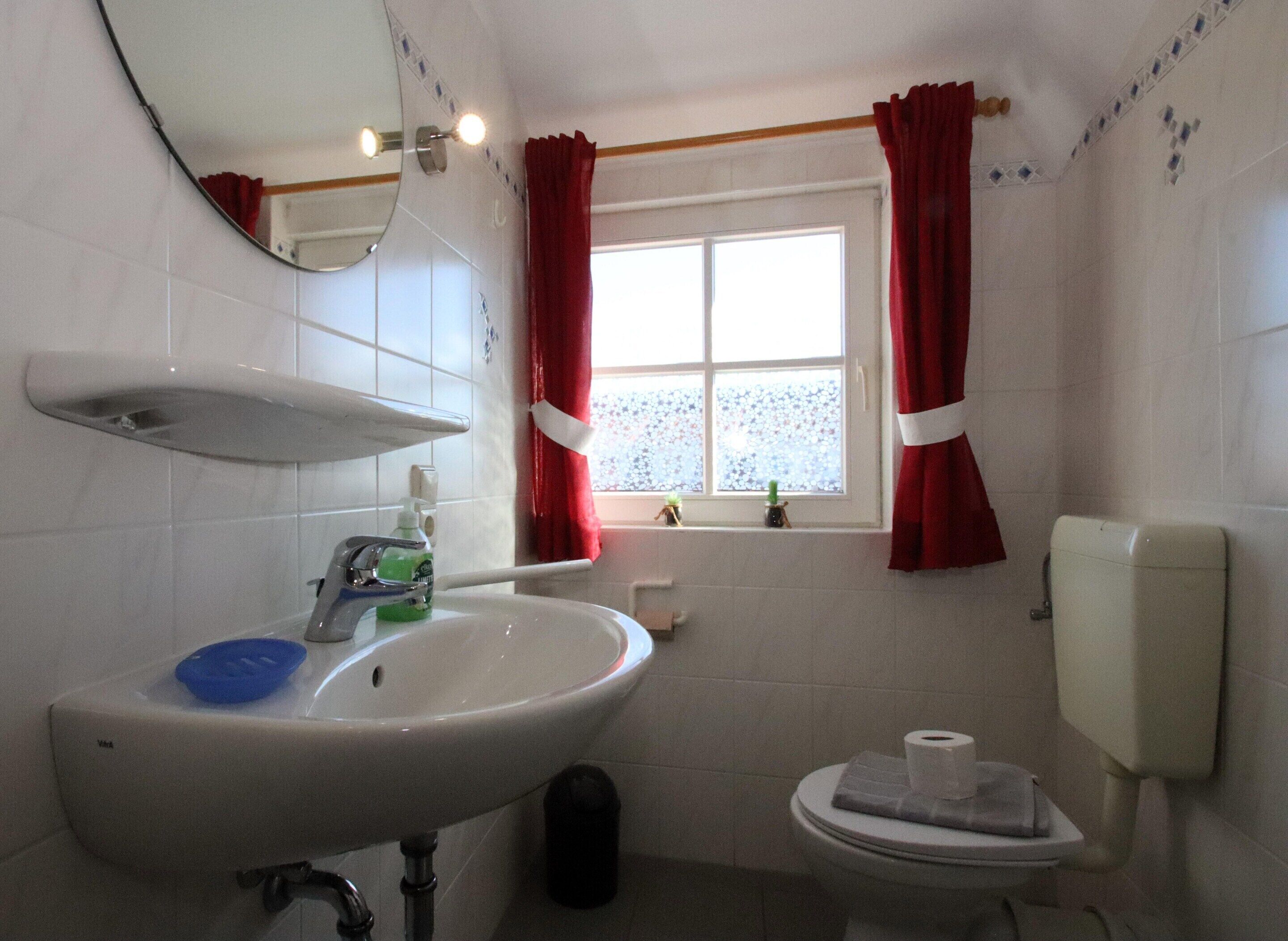 A bathroom with a sink, mirror, toilet, and window with curtains.