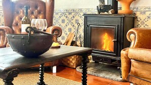 Un salon chaleureux avec une cheminée, des fauteuils en cuir, une table à manger agrémentée d’un saladier et de verres à vin, et un téléviseur fixé au mur.