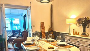 Un coin repas avec une table ronde dressée pour quatre personnes, un lustre et un vase de fleurs posé sur une console.