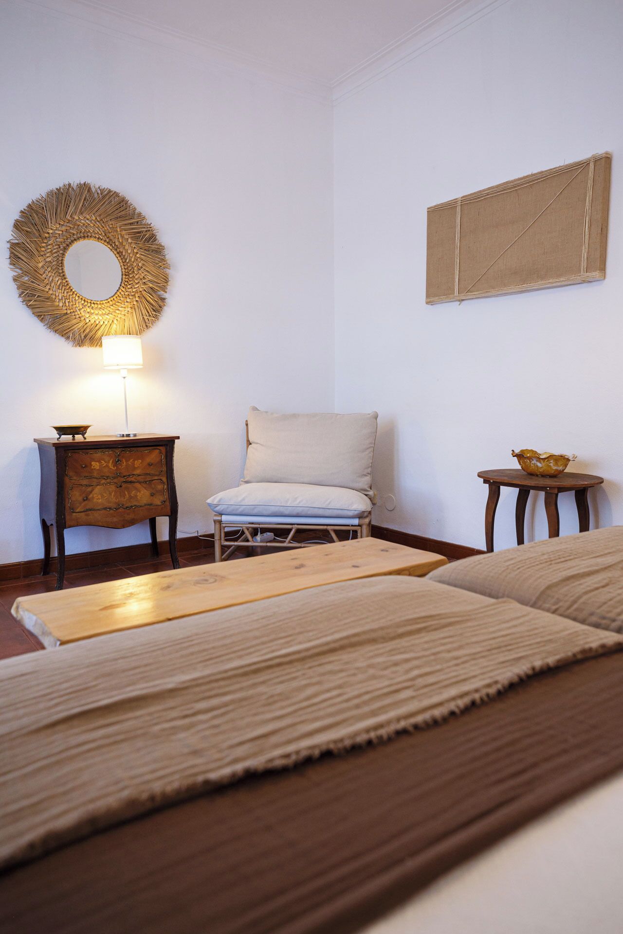 A room with a bed, a chair, a small table, a lamp, and a wall decoration.