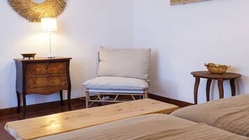 A room with a bed, a chair, a small table, a lamp, and a wall decoration.