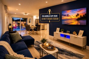 A modern living room with a sofa, dining table, and chairs, a TV, and a wall-mounted sign indicating the FIFA World Cup 2026 location. - FIFA World Cup 2026 Stay Near Miami Stadium (Pompano Beach)