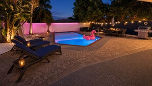 A swimming pool with lounge chairs and a flamingo float, surrounded by palm trees and a barbecue area. - 5 Star Tropical Pool Near Beach & FLL (Pompano Beach)