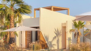 A modern building with a wooden structure, surrounded by desert plants and palm trees. - Casa Tove, a cosy Bungalow in El Pescadero with wifi, yoga deck and pool. (El Pescadero)