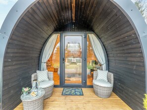 Eine gemütliche, halboffene Holzkonstruktion mit zwei Korbstühlen und einem kleinen Tisch, einer Glastür, die zu einem Schlafzimmer führt, und einem Holzboden.