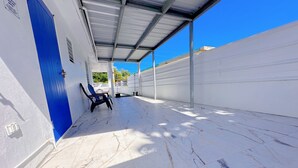 A covered outdoor area with a blue door, a chair, and a white wall with a sign.