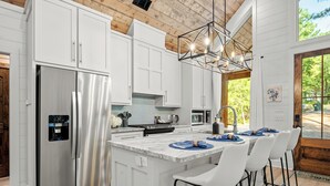 A modern kitchen with white cabinetry, stainless steel appliances, and a bar area with white bar stools.