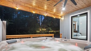 A hot tub with a wooden deck and a large window overlooking a forested area.
