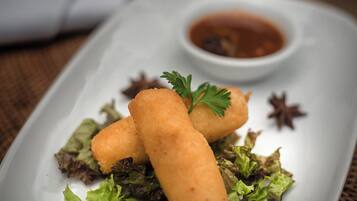 Um prato retangular branco com três itens fritos dourado-acastanhados, uma pequena tigela de molho e um toque de folhas verdes.
