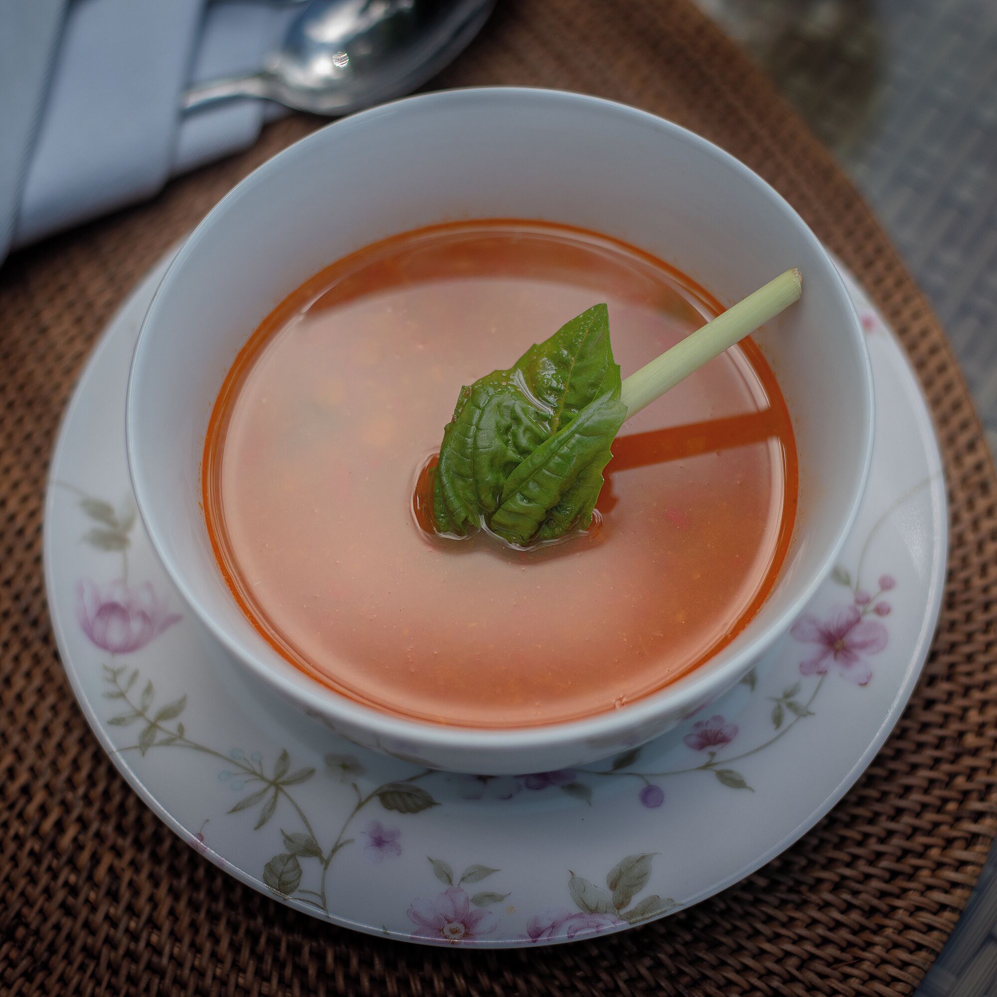 Un tazón de sopa decorado con una hoja verde sobre un plato estampado con motivos florales.