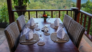A dining table set for four with wicker chairs, a vase with flowers, and a scenic view. - Loid's di Lempuyang (Karangasem)
