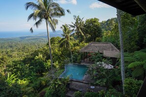 A pool area with a thatched-roof structure, surrounded by lush greenery and a view of the ocean. - Loid's di Lempuyang (Karangasem)