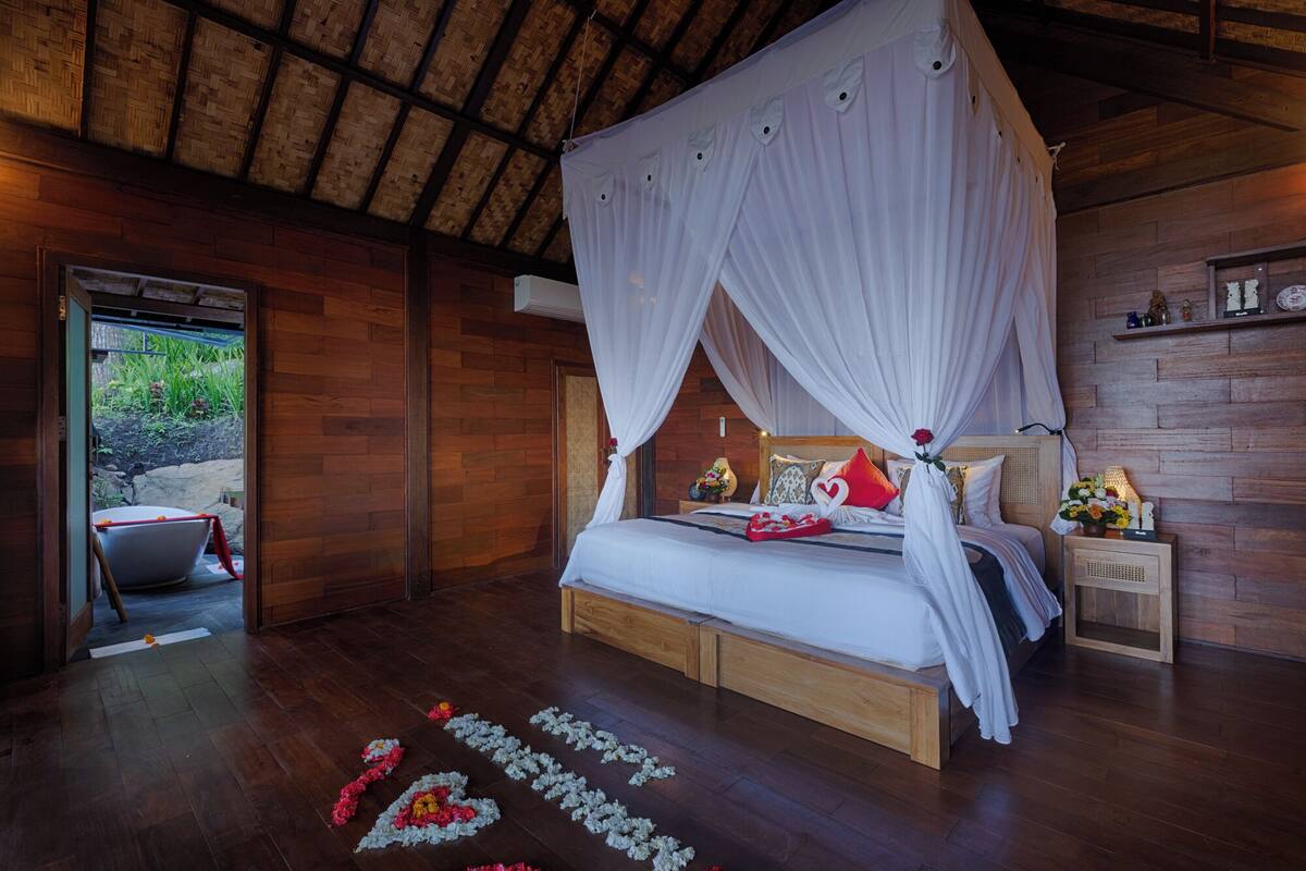 A bedroom with a canopy bed, wooden flooring, and a view of the outdoors.