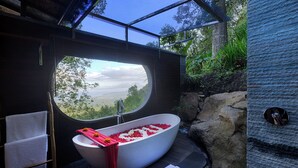 A modern bathroom with a freestanding bathtub, a towel rack, and a view through a large window. - Loid's di Lempuyang (Karangasem)