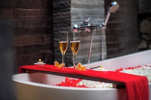 A bathtub with two glasses of champagne, red bath mat, and flower petals. - Loid's di Lempuyang (Karangasem)