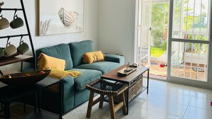 A modern living room with a teal sofa, a coffee table, a black shelf with mugs, a large window, and a ceiling light. - Vacation apartment in Torrox-Park. Modern, bright, cozy, quiet, dogs welcome. (Torrox)
