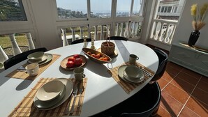 A dining table set with plates, bowls, and cutlery, with a view of the sea and buildings through large windows. - Vacation apartment in Torrox-Park. Modern, bright, cozy, quiet, dogs welcome. (Torrox)