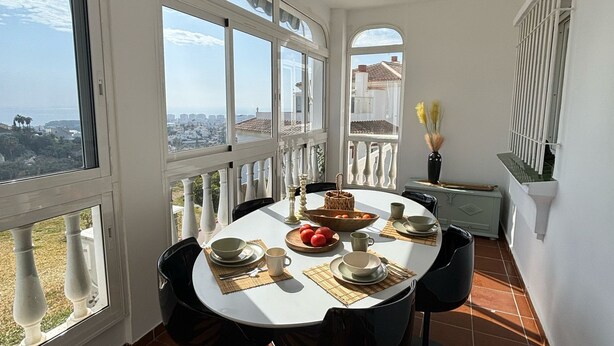 A dining area with a round table set for four, large windows, and a view of the cityscape. - Vacation apartment in Torrox-Park. Modern, bright, cozy, quiet, dogs welcome. (Torrox)