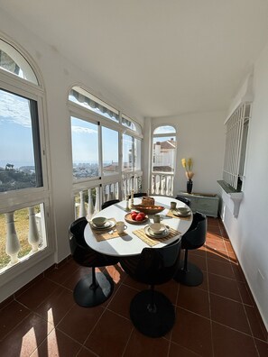 Un coin repas avec une table ronde dressée pour quatre personnes, de grandes fenêtres et une vue sur le paysage urbain.