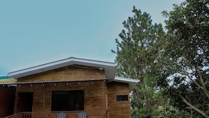 A modern wooden house with a balcony, large windows, and a view of surrounding trees.