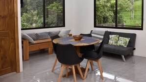 A dining area with a round table, black chairs, a wooden bench, and a grey sofa.