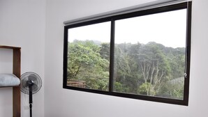 A bedroom with a large window, a standing fan, and a wooden shelf.