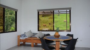 A dining area with a wooden table, black chairs, and a view of a grassy field with cows.