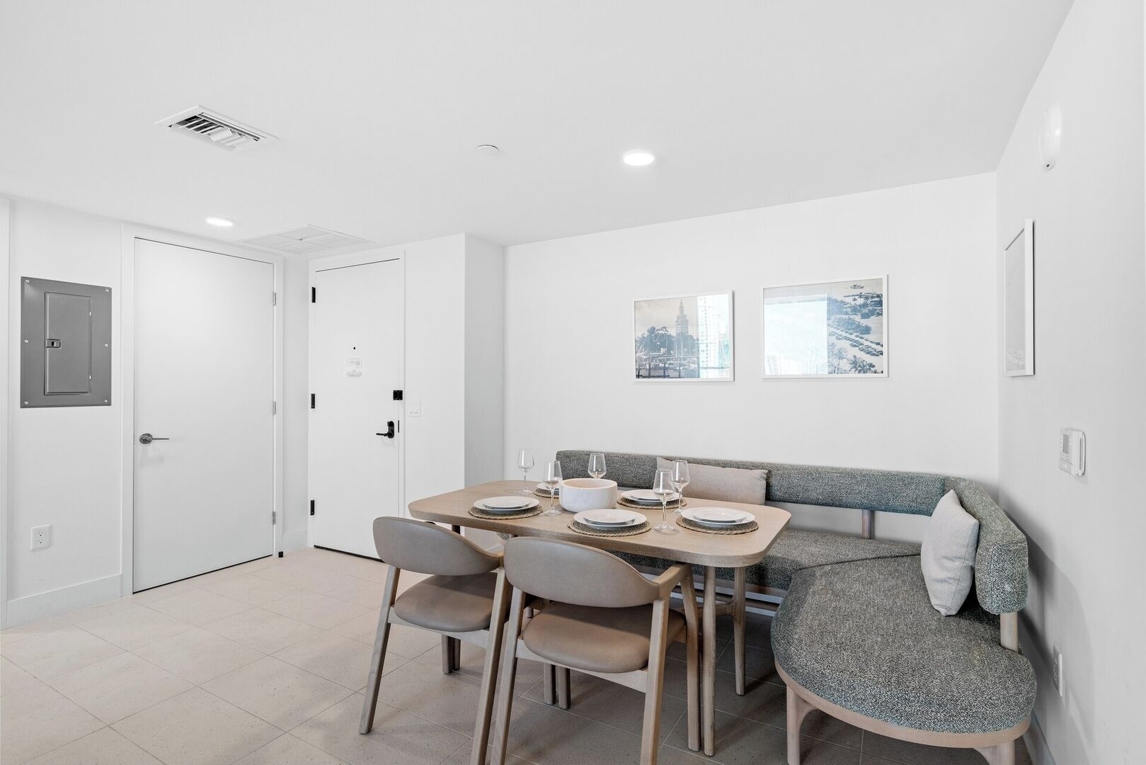 A dining area with a table set for four, two chairs, a bench, and a white door with a small window.