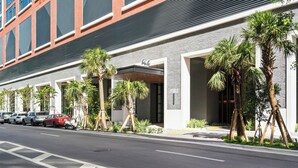 Un hotel con fachada moderna, palmeras y automóviles estacionados a lo largo de la calle.