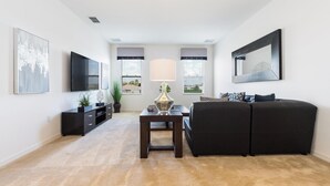 A modern living room with a dark sofa, a flat-screen TV, a coffee table, and a lamp. - ⛱ Providence Resort - 5★ Golf Community - Lakeview Home – Communal Amenities☀ (Davenport)