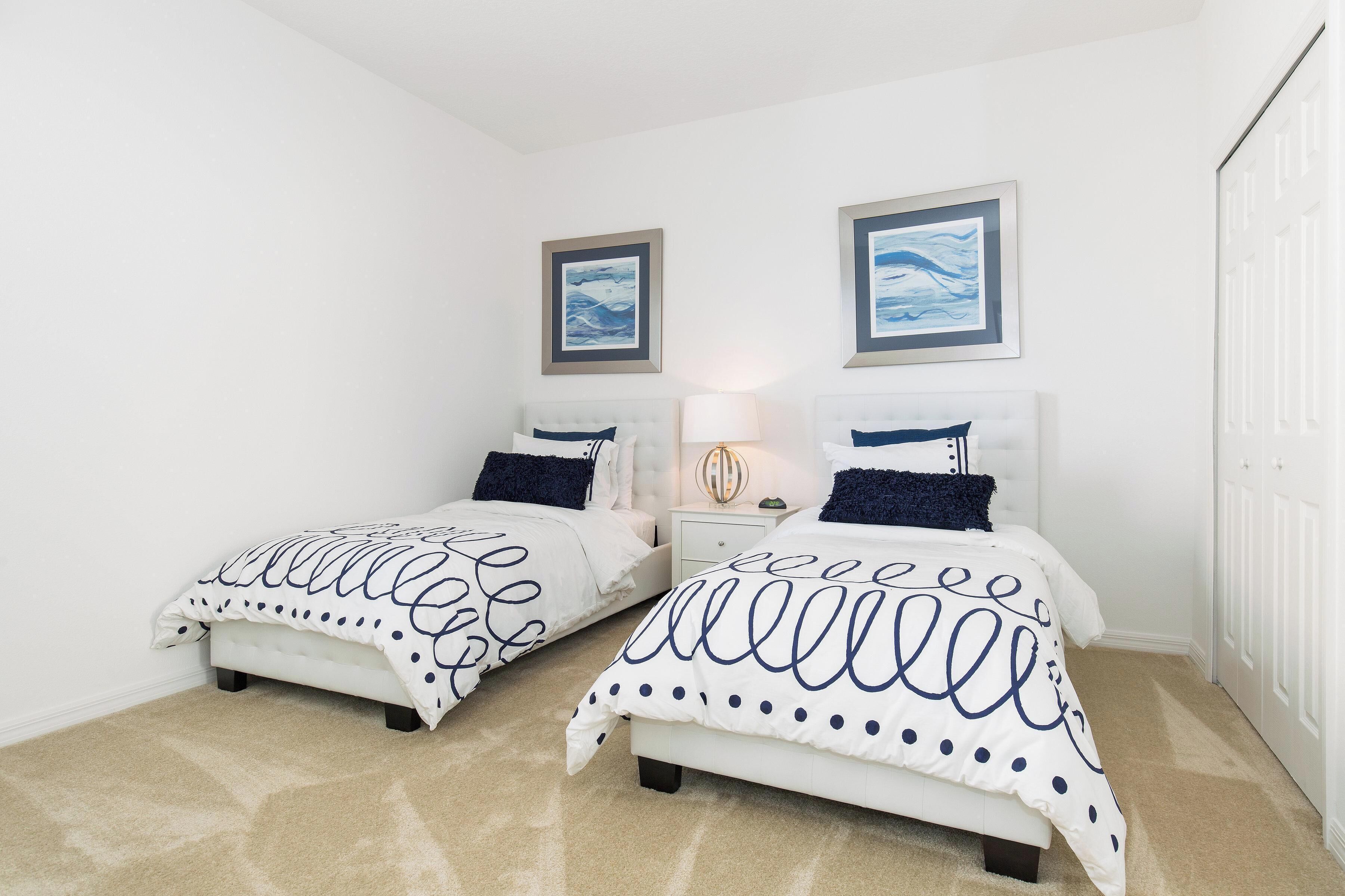 A bedroom with two beds, white walls, and framed artwork above the beds.