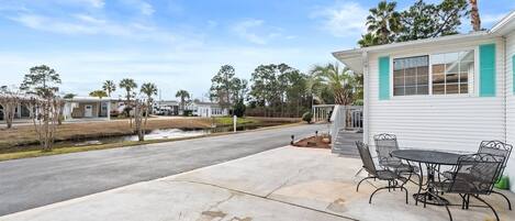 A residential property with a paved driveway, a patio with outdoor furniture, and a white building with green shutters.