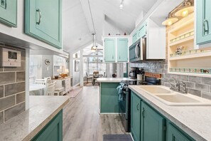 A kitchen with teal cabinetry, a central island, and a dining area with white chairs. - 3b 3ba Home, Pet allowed, 2 Pools, Hot Tub, Gym (Panama City Beach)