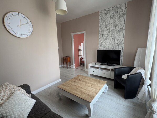 A living room with a wooden coffee table, a sofa, a TV on a white stand, and a clock on the wall. - Bright apartment near the quays, perfect for exploring Quimper! (Quimper)