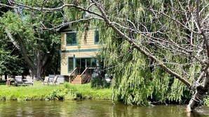 Une maison située au bord d’une rivière, offrant une vue dégagée sur l’eau et la végétation environnante.