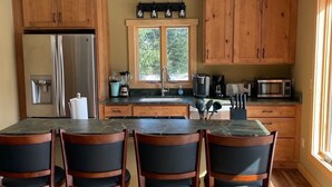 Une cuisine moderne avec des meubles en bois, un réfrigérateur en acier inoxydable, un évier à deux bacs et un coin bar avec des tabourets.