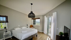 A bedroom with a bed, a bedside table, a lamp, a chair, a TV, and large windows. - Luxury 8-person Villa with pool and sea view (Soalheira)