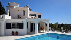 A white villa with a pool, outdoor seating, and a view of the hills. - Luxury 8-person Villa with pool and sea view (Soalheira)
