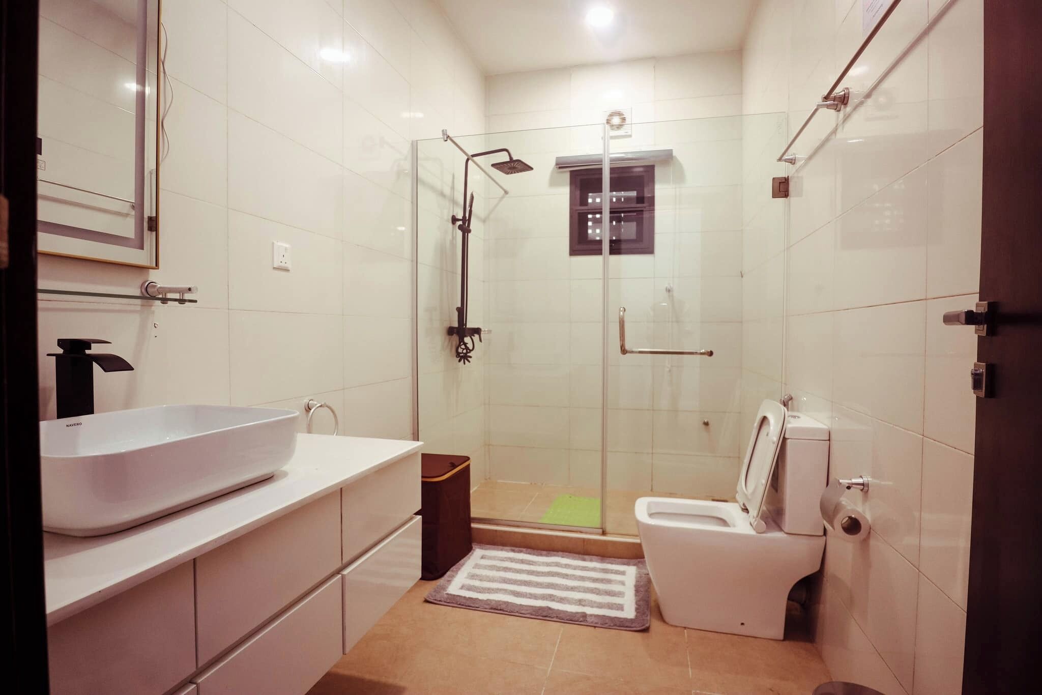 Une salle de bain moderne avec un grand lavabo blanc, des toilettes et une douche séparée par une paroi de verre.
