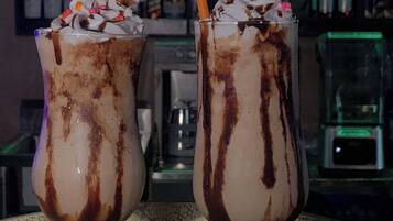 Deux milkshakes garnis de crème fouettée et de sirop au chocolat, servis dans de grands verres avec une paille, sur le comptoir d’un bar.