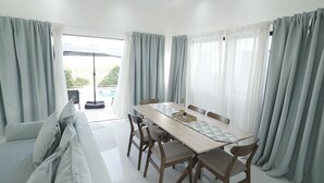 A dining area with a wooden table, six chairs, and a sofa with light grey cushions.